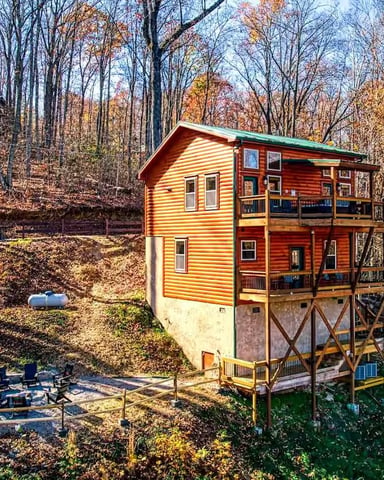 Yellow and red elevated cabin in autumn forest with fire pit and bare trees