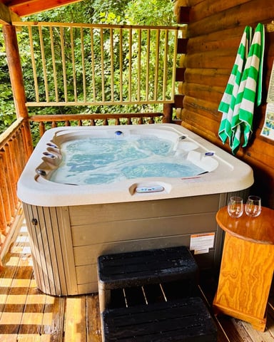 Hot tub with blue water on wooden deck surrounded by log cabin walls and green striped towels