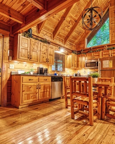 Wooden cabin kitchen and dining area with exposed beam ceiling, stained glass door, and forest views through large windows