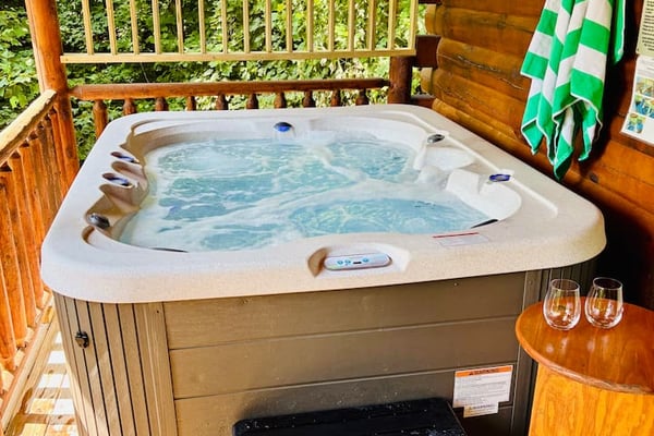 Hot tub with bubbling water on wooden deck surrounded by log cabin walls and green striped towels